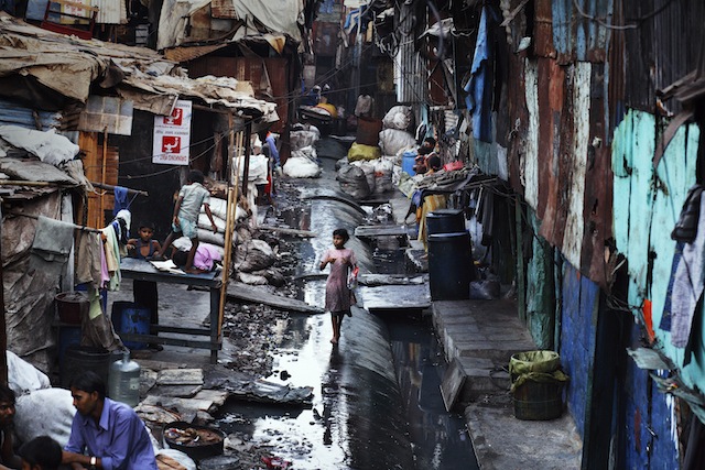 "THE PLACES WE LIVE",  Jonas Bendiksen. girl walks along a water pipe in the Industrial Area of Dharavi. Although it functions as a throroughfare through this area of the slum, the water in the pipes is headed for the more affluent southern areas of the city. Mumbai. India. 2006.  