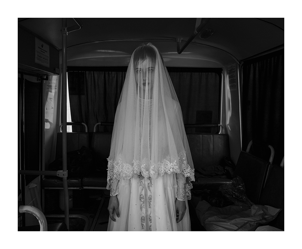 Davide Monteleone VII Photo for the Carmignac FoundationRepublic of Chechnya, Russia, 03/2013. Rada, 14 years old is trying a wedding dress designed by her sister, inside a bus during the rehearsal for the shooting of a movie on Chechen deportation. Child brides were very common in the Chechen tradition as in many other Muslim countries. Despite President Kadyrov is strongly promoting a revival of Chechen tradition and Islamic law, he was recently forced by central authority of the Russian Federation to publicly condemn the practice of child marriage, illegal in the entire Russian Federation. Shatoy.