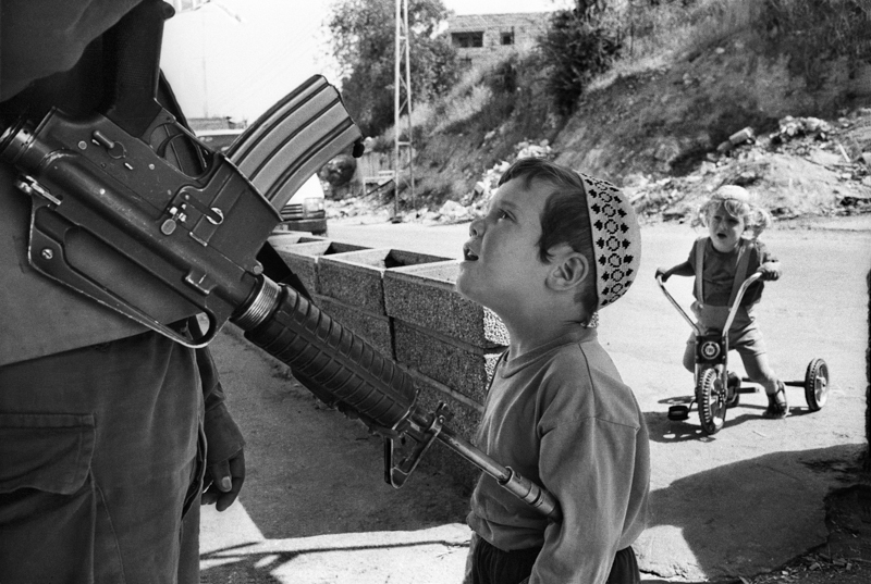Un bambino e il soldato armato di M16 a guardia dell'insediamento dei coloni israeliani oltranzisti di Bet Hadassa nel centro di Hebron a ridosso delle case abitate da palestinesi