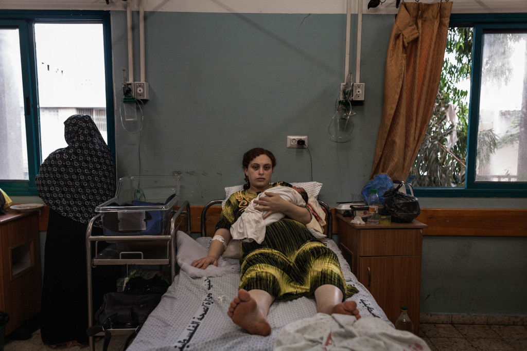 Maysa holds her newborn baby boy and 4th child in her arms as she recovers in a bed at the Maternity ward in Gaza city while a relative looks out the window onto the hospital morgue where corpses are prepared for funeral during Operation Protective Edge in the Gaza strip.