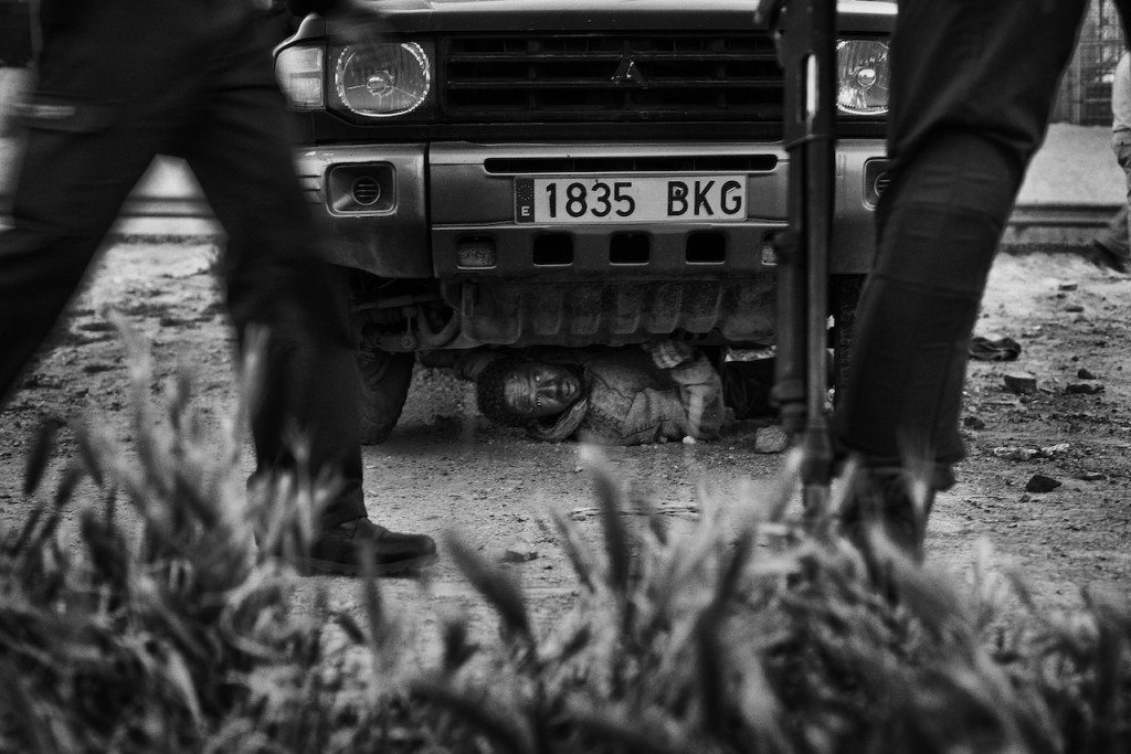 Melilla, Spagna, aprile 2014. Un migrante subsahariano si nasconde sotto un veicolo nel tentativo di evitare un espatrio forzato da parte della Guardia Civil.  Alla fine è riuscito a sfuggire alla cattura. Melilla, Spain, April 2014. A subsaharan migrant hides himseld under a vehicle trying to avoid a forced expatriation by the Guardia Civil. He eventually managed to escape capture. © Gianfranco Tripodo / Contrasto Melilla, Spain, April 2014. Some 20 subsaharan migrants manage to escape from the Police and start running through the fields next to the border.  ©Gianfranco Tripodo / Contrasto 