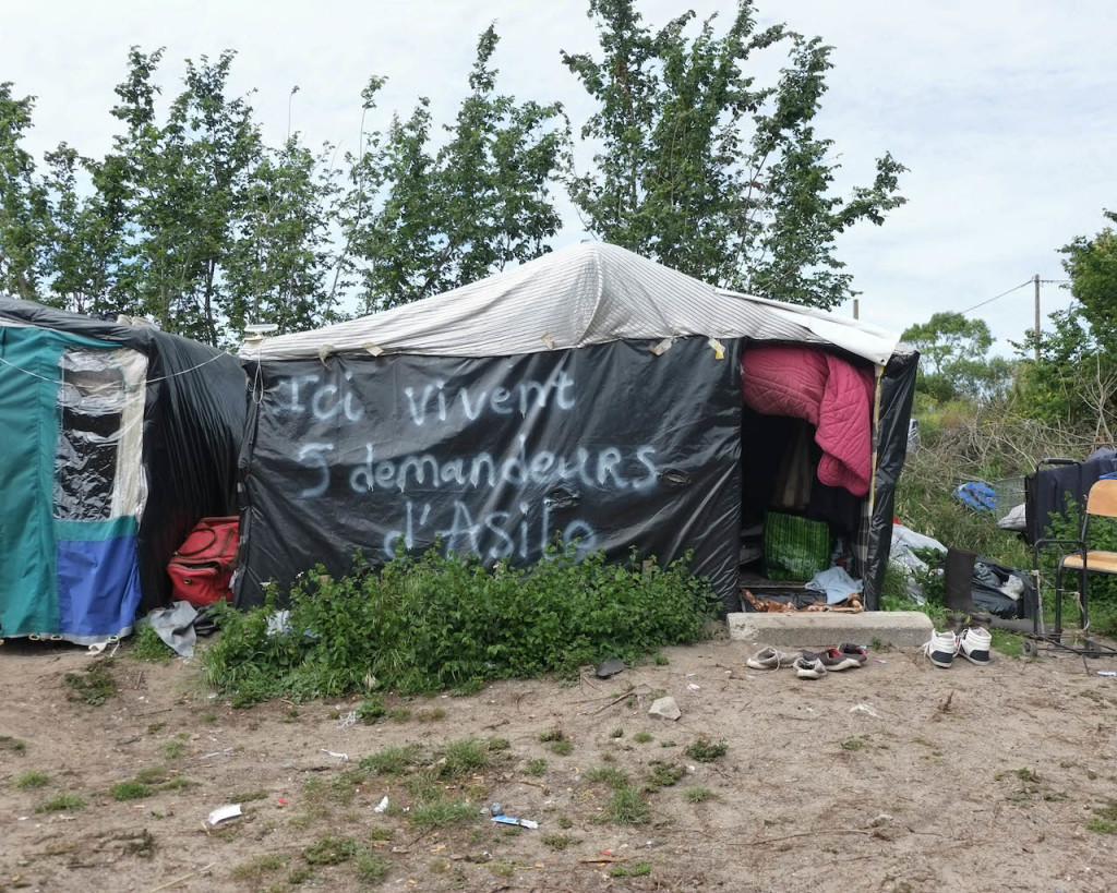 One of the first Sudanese building, situated in the most ancient Sudanese neighbourhood in the western part of the camp. It may host up to five people. The writing on the wall says "Five asylum seekers live here" (June 2015, "New Jungle" refugee camp, Calais, France)