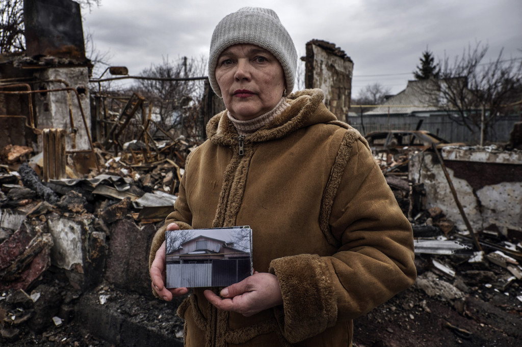 Vera Andreyvna  mostra una foto della sua abitazione scattata prima che questa fosse colpita da una bomba al fosforo. Ogni giorno Vera fa visita ai suoi cani che ancora vivono nel cortile della casa per nutrirli ed accudirli.