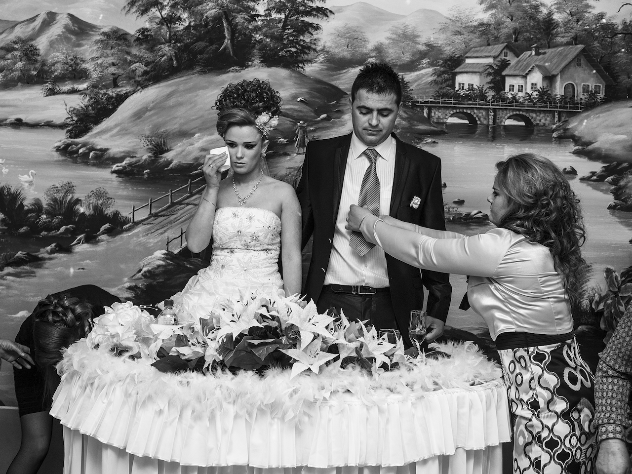 Last preparations at a wedding party. The sister of the groom adjusts his neck tie. In a moment of what should have been happiness, the bride holds back tears. The marriage means she has to abandon her relatives. Her husband is an immigrant from Italy and she will have to follow him there.Many Albanian expatriates ask from their relatives back home to find them local brides. In that case, marriage means immigration.Tirana, Albania, 2012