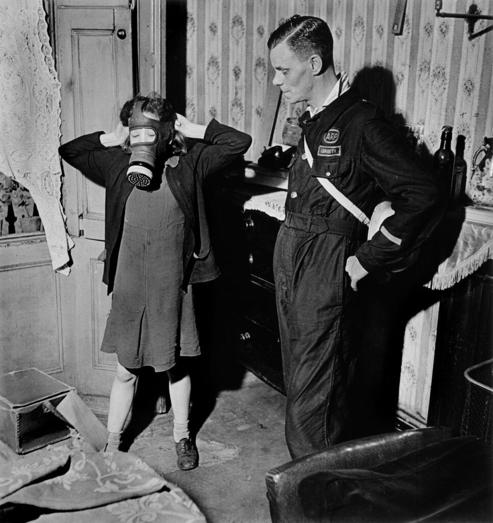 GB. London. June-July 1941. Civil-defense worker showing girl how to wear a gas mask. © Robert Capa © International Center of Photography / Magnum Photos